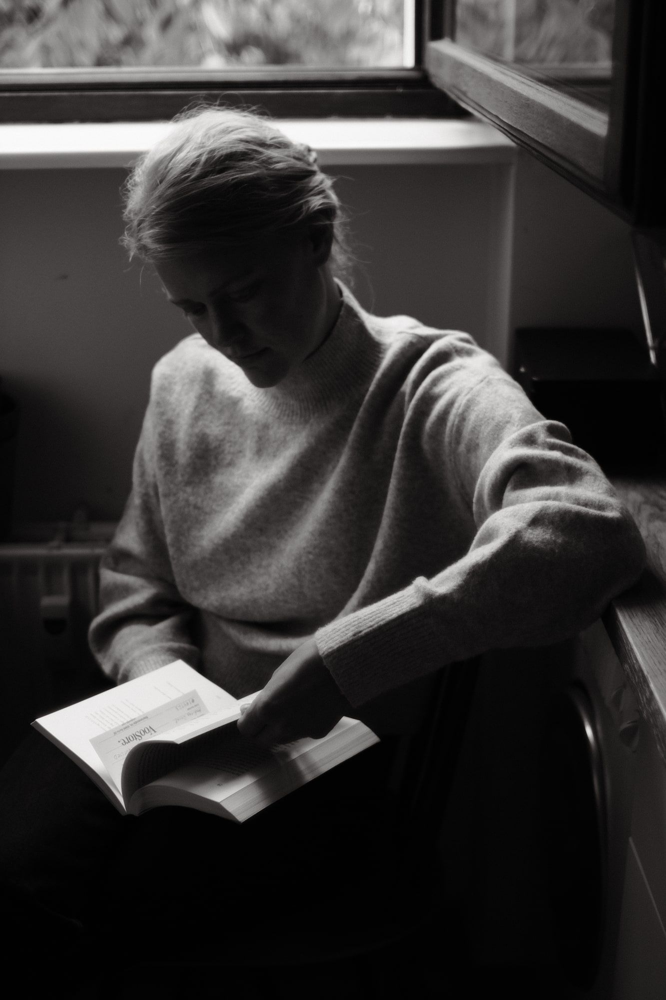 Sort-hvid fotografi af Karen Tortzen, der sidder ved et vindue og læser i en bog